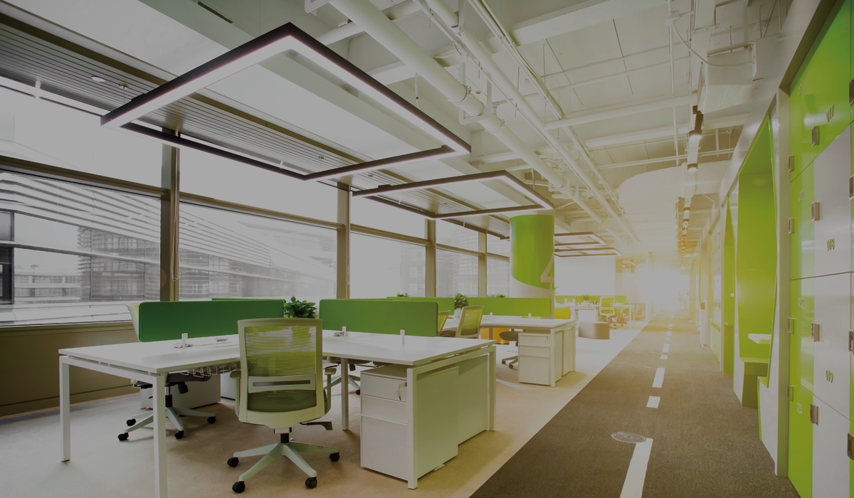  An open office space with bright green accents, white desks and chairs, and large windows looking out onto a city skyline; inspirational artwork adorns the walls.